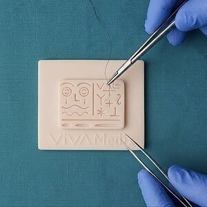 Gloved hands practicing microsurgery with fine forceps on the VivaMedix MicroSuture pad